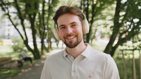 happy runner jogger smiling man put on wireless headphones earphones enjoy music in park outdoors