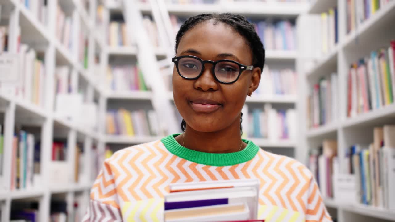 Young Black Woman Holding Books and Smiling in a Library