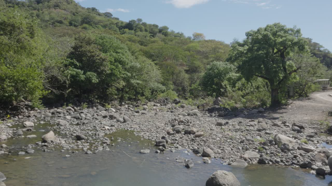 el cambio climático afecta a un río en honduras, secando su flujo de agua durante la temporada de verano, un paisaje con muchas rocas y árboles frondosos