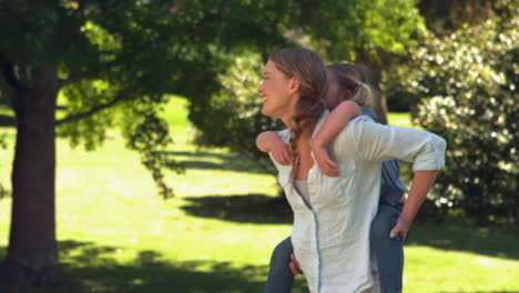 young mother giving her daughter a piggy back in the park