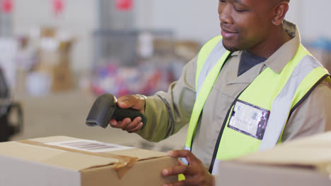 african american male worker wearing safety suit and scanning boxes in warehouse