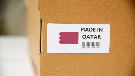 hands applying made in qatar flag label on a shipping cardboard box with products