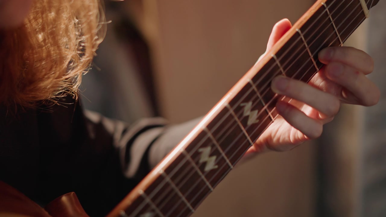 Closeup of guitar playing. Teacher guides guitarist during intimate fingerstyle practice session. Detailed closeup of musician demonstrating accurate fretting under studio lighting conditions