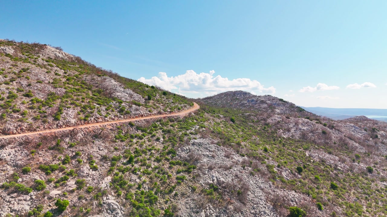 Drone ascends above a remote dirt track at the foot of the Velebit mountains, revealing the wide, rugged wilderness of Zadar County under clear skies and bright sun.