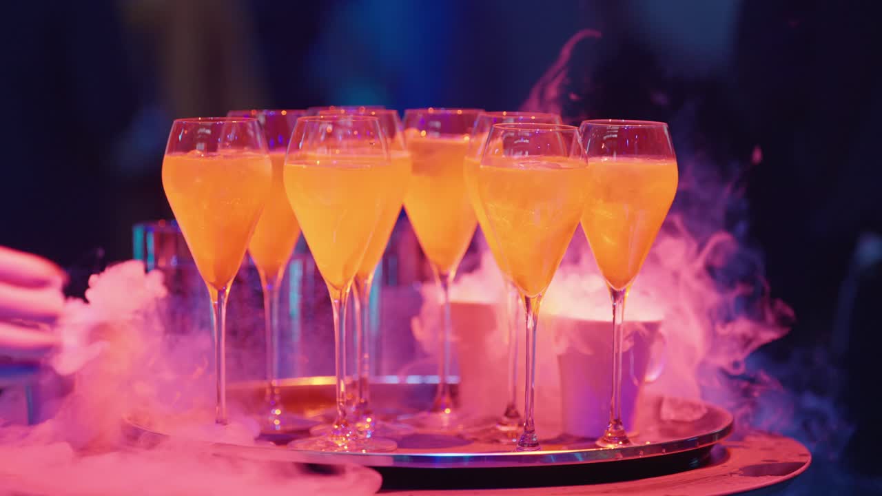 People taking glowing orange cocktails from a tray with dry ice smoke at a party