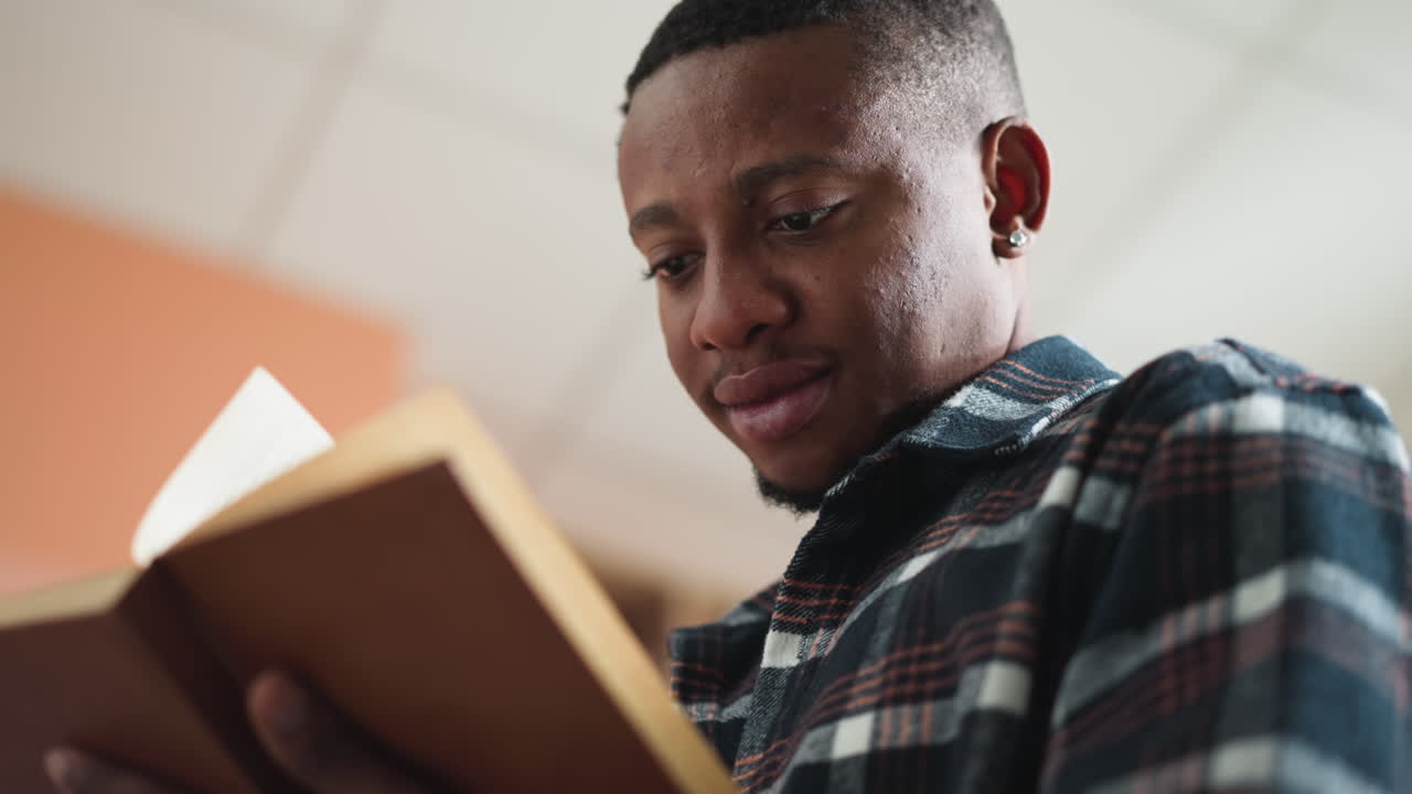Dark-skinned man learns literature in library. College student reads educational literature in campus bookstore as part of exam preparation. Guy reads story
