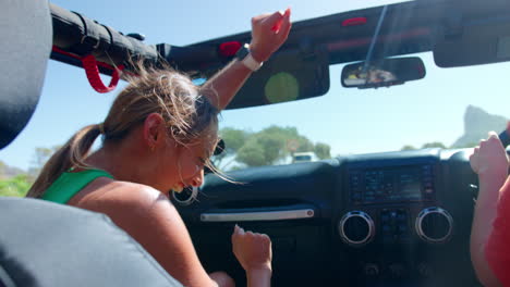 group of laughing female friends having fun in open top car on road trip