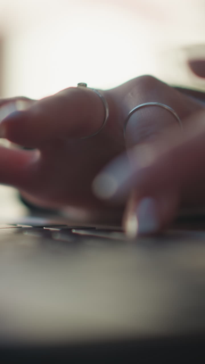 primo piano di dita eleganti con anelli che scrivono sulla tastiera del portatile, mostrando unghie lucidate in un ambiente esterno rilassato, messa a fuoco morbida sul portatile, con sfondo sfocato