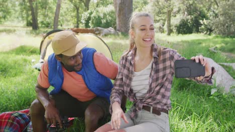 Happy-diverse-couple-camping-and-taking-selfie-with-smartphone-in-park,-slow-motion