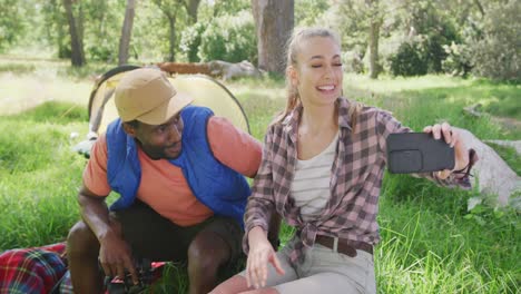 pareja feliz acampando y tomando selfies con teléfonos inteligentes en el parque, cámara lenta