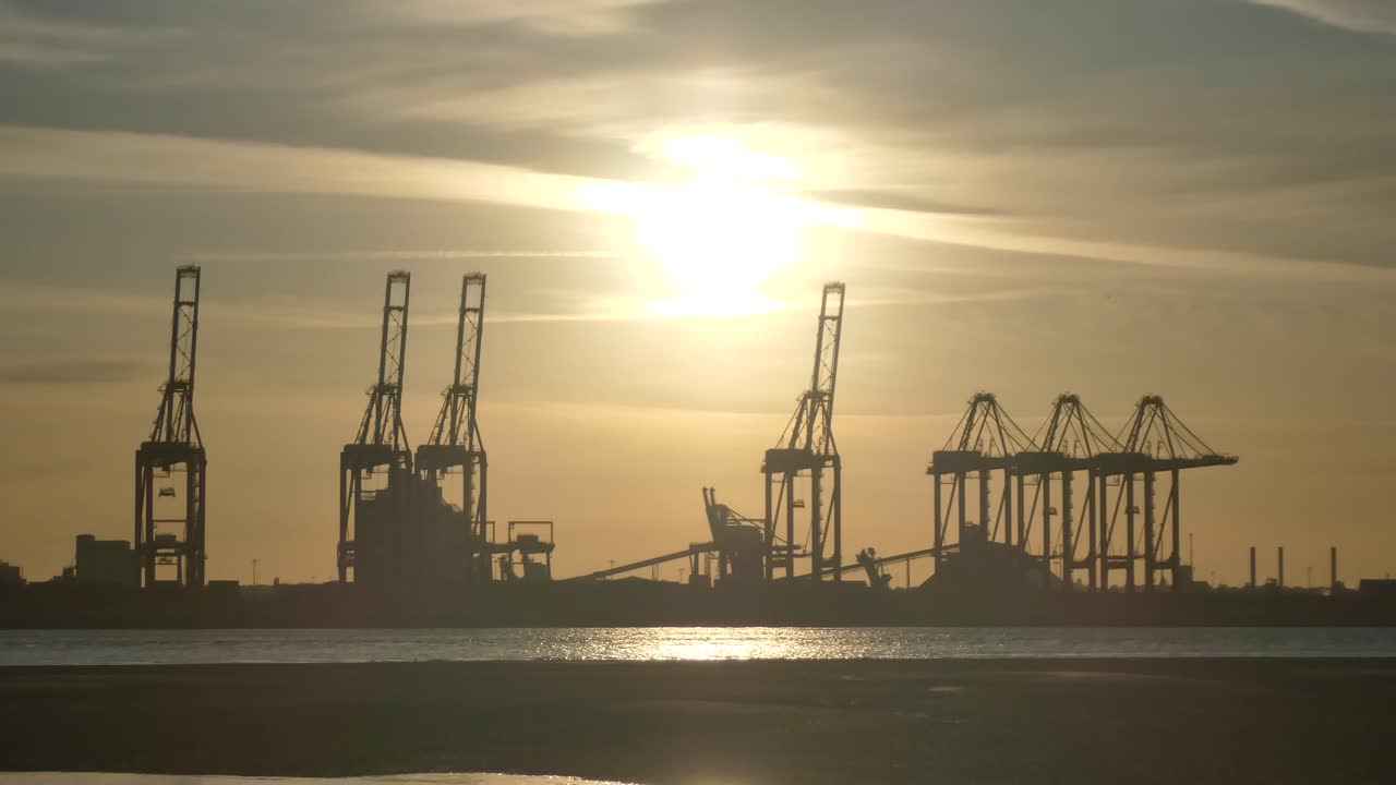 Silhouette shipping port cargo loading cranes on shimmering sunrise water three of five