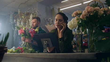 female florist talks by phone with customer and uses tablet