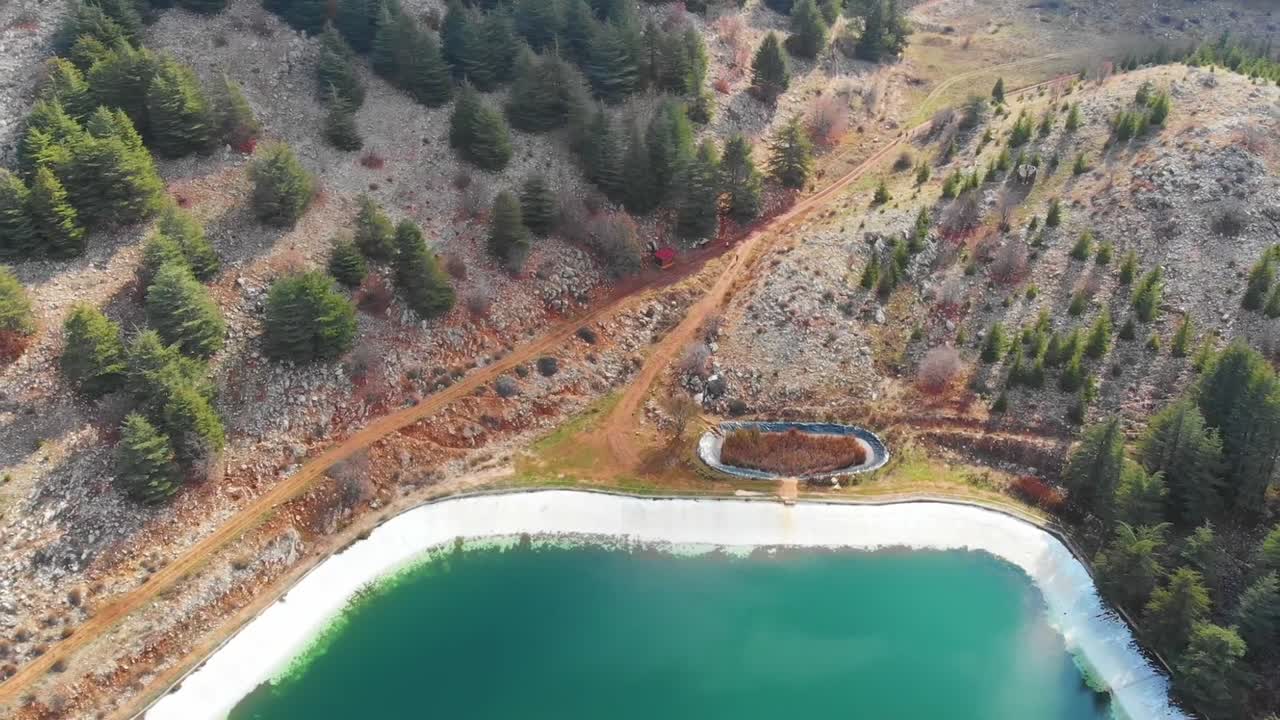 Drönarvideo ovanifrån som visar formen av Barouksjön omgiven av träd och oländig terräng i Libanon. Perfekt för kampanjer inom miljö, turism och friluftsliv.