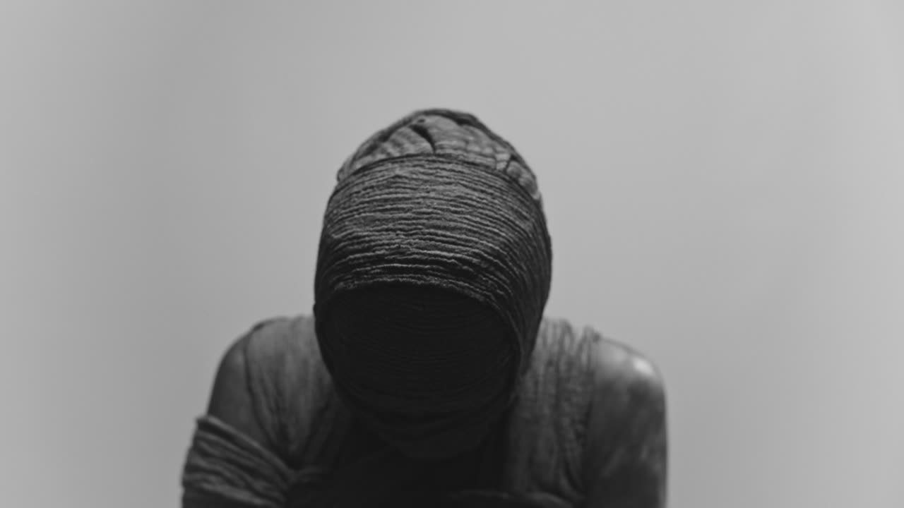 A mummy of a woman on a white backdrop keeps her head down