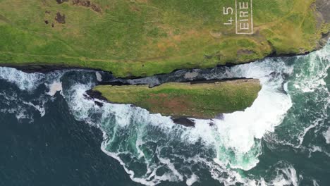 rolling aerial view of rugged coastline with 'éire' sign, waves crashing against cliffs