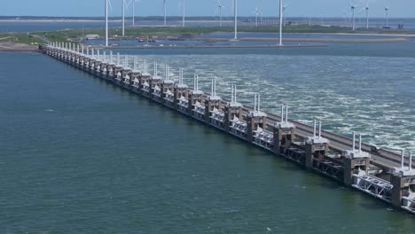 The-Oosterscheldekering-with-in-the-background-windturbines-during-daytime,-aerial