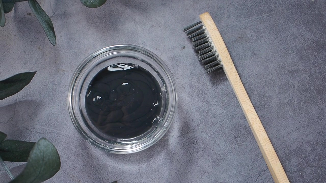 Bamboo Toothbrush and Bowl of Charcoal Toothpaste on Grey Surface