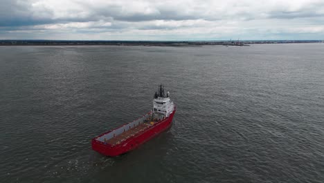 an aerial view of a red ship sailing on a tranquil sea on a cloudy day