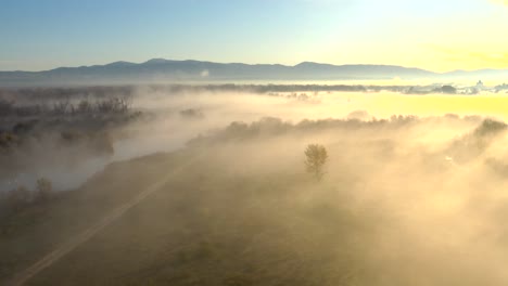 aerial over farm land and a pond with thick fog during a bright sunrise