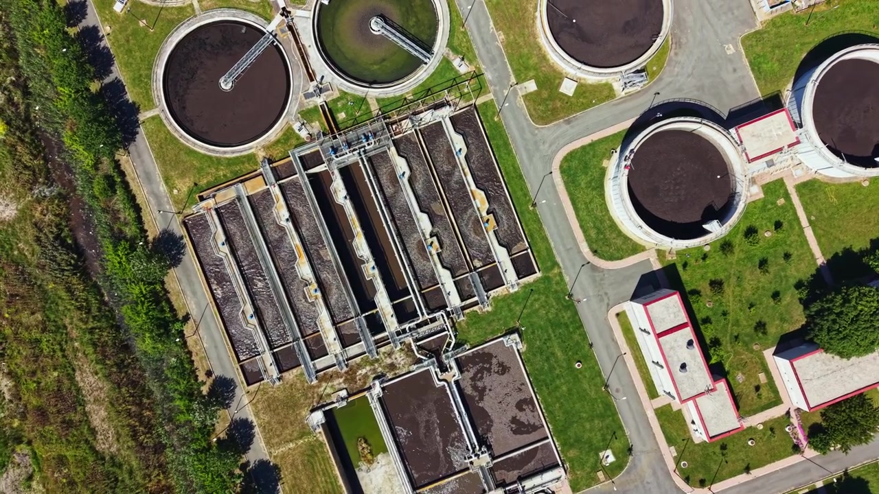 Wastewater treatment facility shows various stages of water processing in an urban area during daylight hours