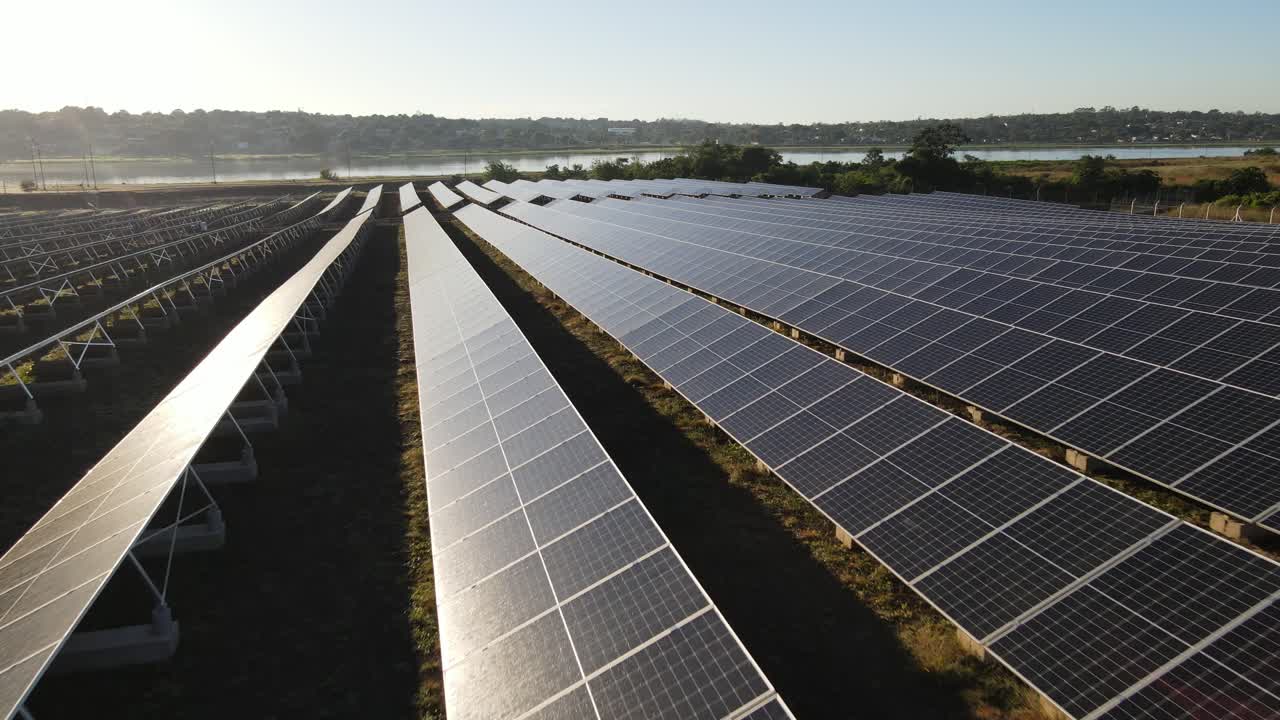 Vista aerea che sorvola lentamente file di pannelli solari fotovoltaici vicino a un fiume di campagna nebbioso.