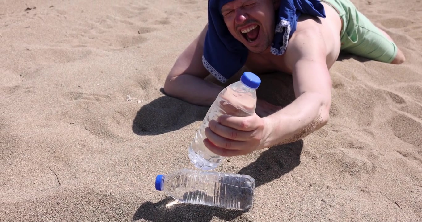Uomo che striscia sulla sabbia del deserto e si protende verso una bottiglia d'acqua di plastica, filmato 4k.