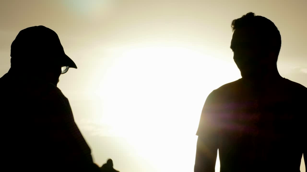 Silhouetted Conversation Between Elder and Younger Man at Sunset