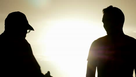 silhouetted conversation between elder and younger man at sunset