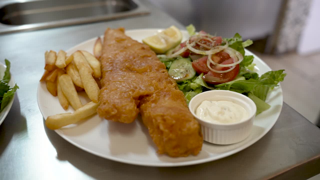 Crispy fried fish served with fresh salad and tangy sauce in a vibrant kitchen setting