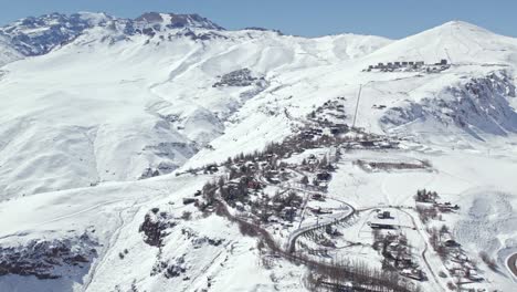 Aerial-view-establishing-the-snowy-mountain-village-of-Farellones-with-the-exclusive-center-of-La-Parva-and-El-Colorado-in-the-background-on-a-sunny-day,-Chile