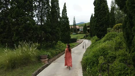 Dama-De-Rojo-Caminando-Por-Un-Sendero-En-Un-Jardín-Botánico-De-Estilo-Italiano-Con-Un-Paisaje-Circundante-En-Ratchaburi,-Tailandia