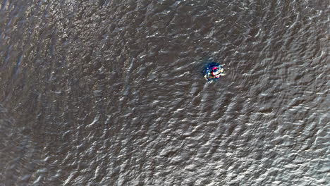 a single diver glides across textured ripples beneath a steady overhead drone, bright gear punctuating the gray surface and conveying training, vigilance, and quiet endurance in open water