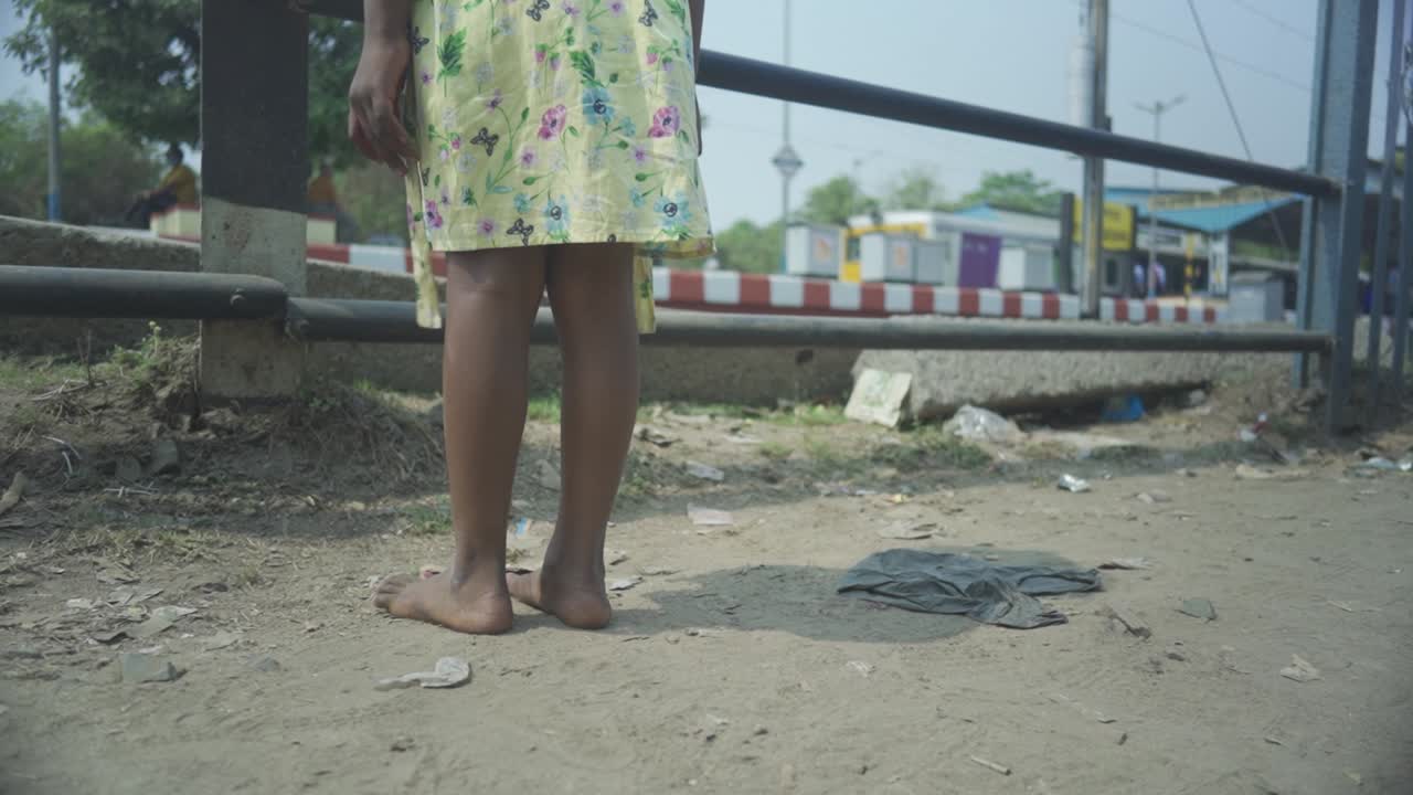 Unrecognized poor Asian dark skin girl walks bare feet and watches train passing by