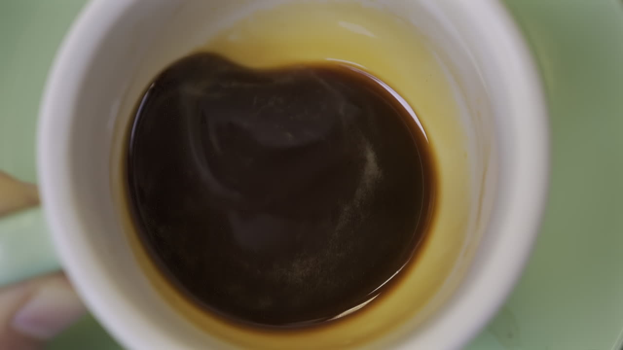 Close up of a man's hand swirling a cup of espresso on a green plate