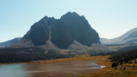 Stunning-aerial-drone-landscape-nature-descending-shot-of-a-large-meadow-with-a-small-stream-with-the-beautiful-Lower-Red-Castle-Lake-and-peak-behind-up-in-the-High-Uinta-national-forest-in-Utah