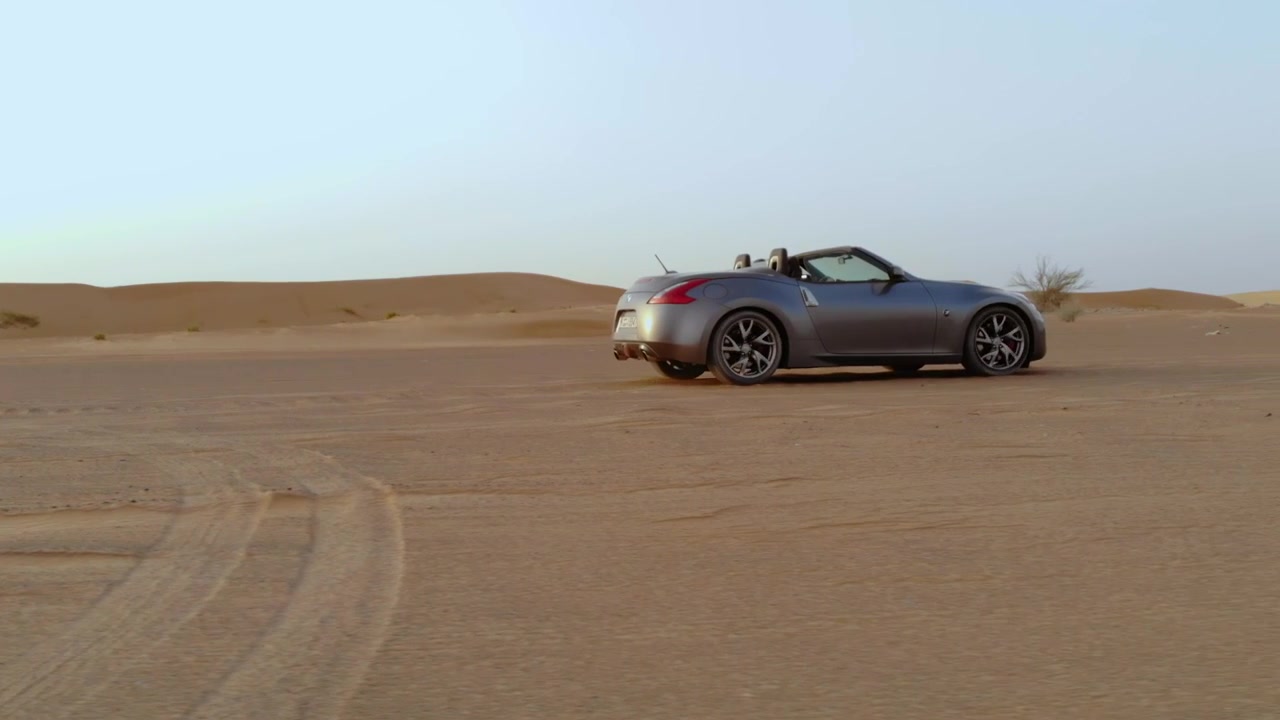 Auto decappottabile nel deserto - ripresa in movimento laterale seguita da drone