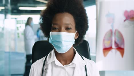 close-up view of african american female doctor in medical mask looking at camera in good mood in hospital