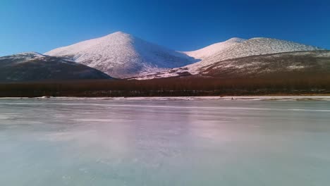 volando un dron sobre un río congelado y un bosque gris en la soleada yakutia
