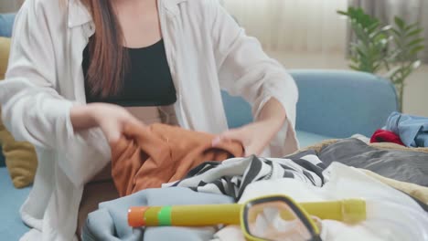 asian young woman packing clothes in suitcase at home, preparing for vacation