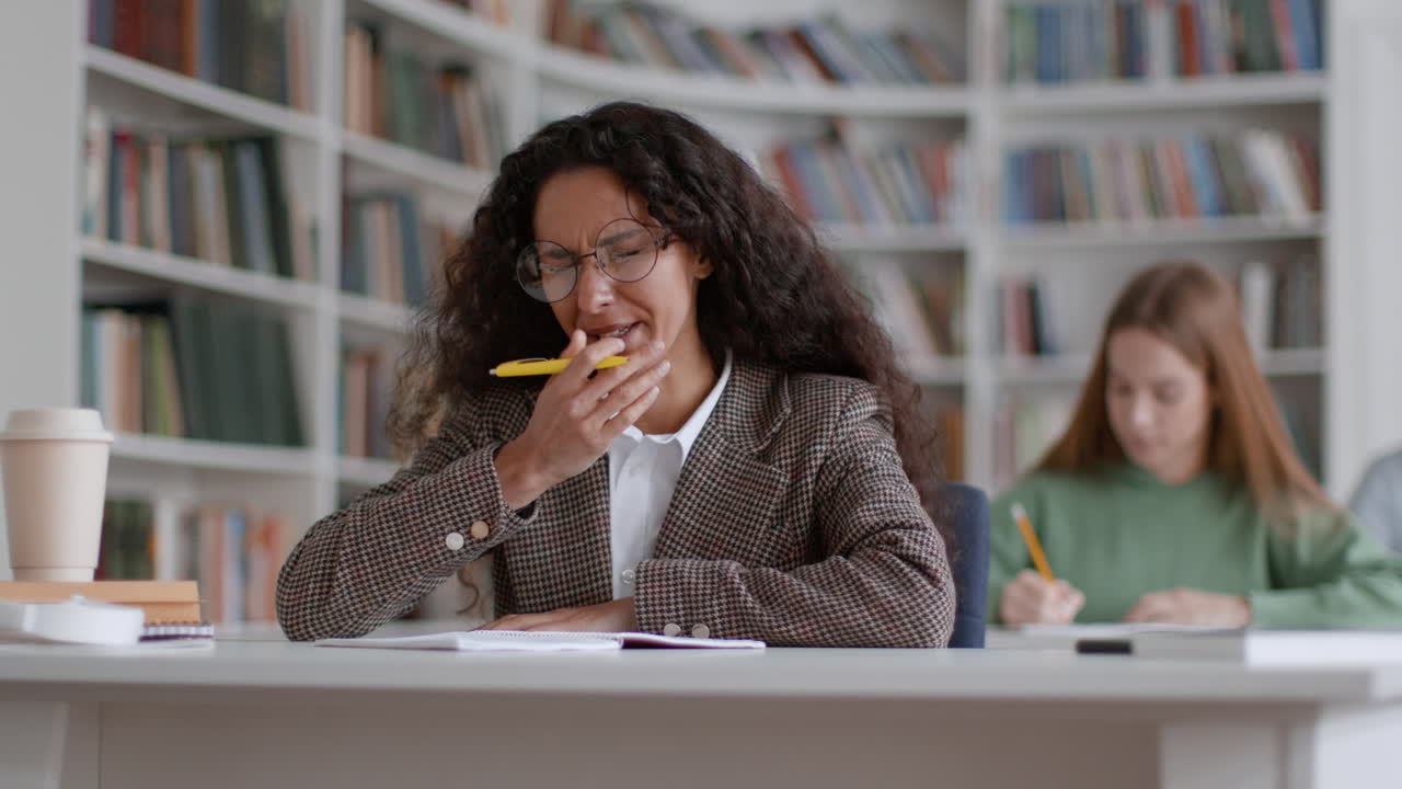 Tired Student Struggles with Exhaustion While Studying in Library