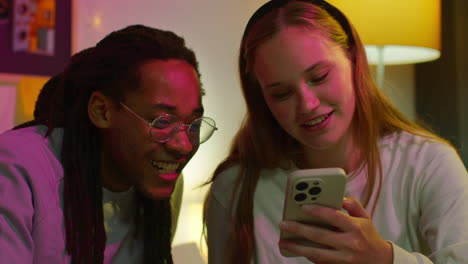 a couple laughing together while looking at a phone.