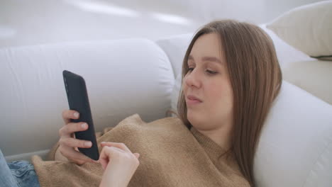 Frau-Liegt-Auf-Der-Couch-Im-Wohnzimmer-Und-Chattet-Mit-Dem-Smartphone,-Um-Eine-Nachricht-Zu-Schreiben.-Einsame,-Glückliche-Dame,-Die-Sich-Mit-Ihrem-Smartphone-Entspannt,-Auf-Der-Couch-Sitzt-Und-Liest,-Schreibt,-Sucht-Und-Im-Mobilen-Internet-Surft