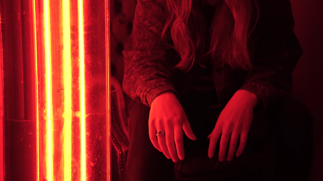 Portrait of a young caucasian female sitting in a bar with orange-red neon lighting