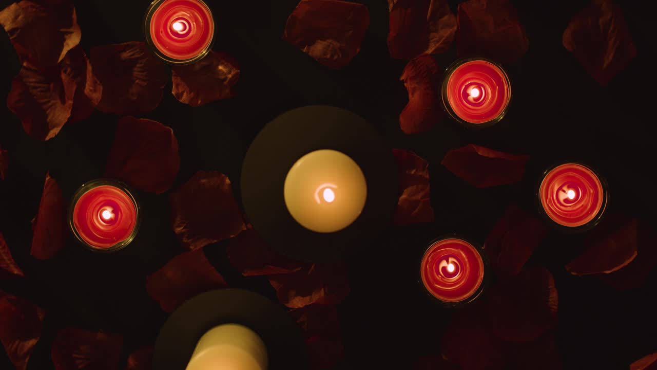 Overhead Shot Of Romantic Lit Red Candles Revolving On Background Covered In Rose Petals