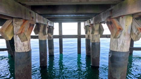 una vista de cerca de la parte inferior de un muelle, que muestra las vigas de soporte de madera y los pilares robustos sumergidos en el agua