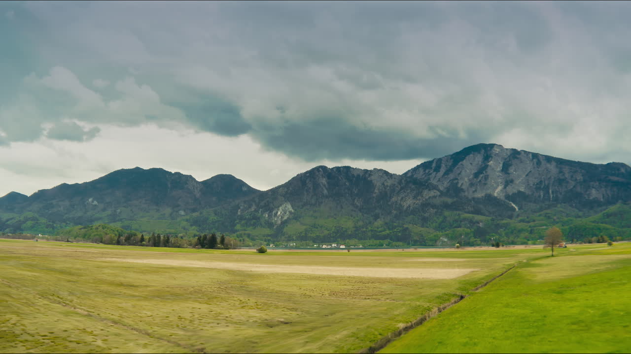 Veduta aerea di prati rigogliosi, maestose montagne con nuvole di pioggia.