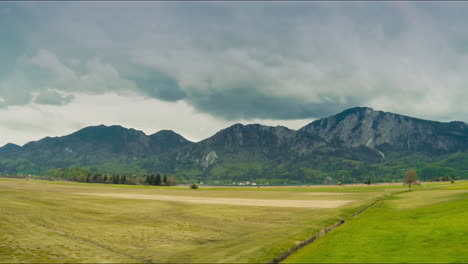 Aerial-of-lush-meadows,-towering-mountains-with-rainclouds