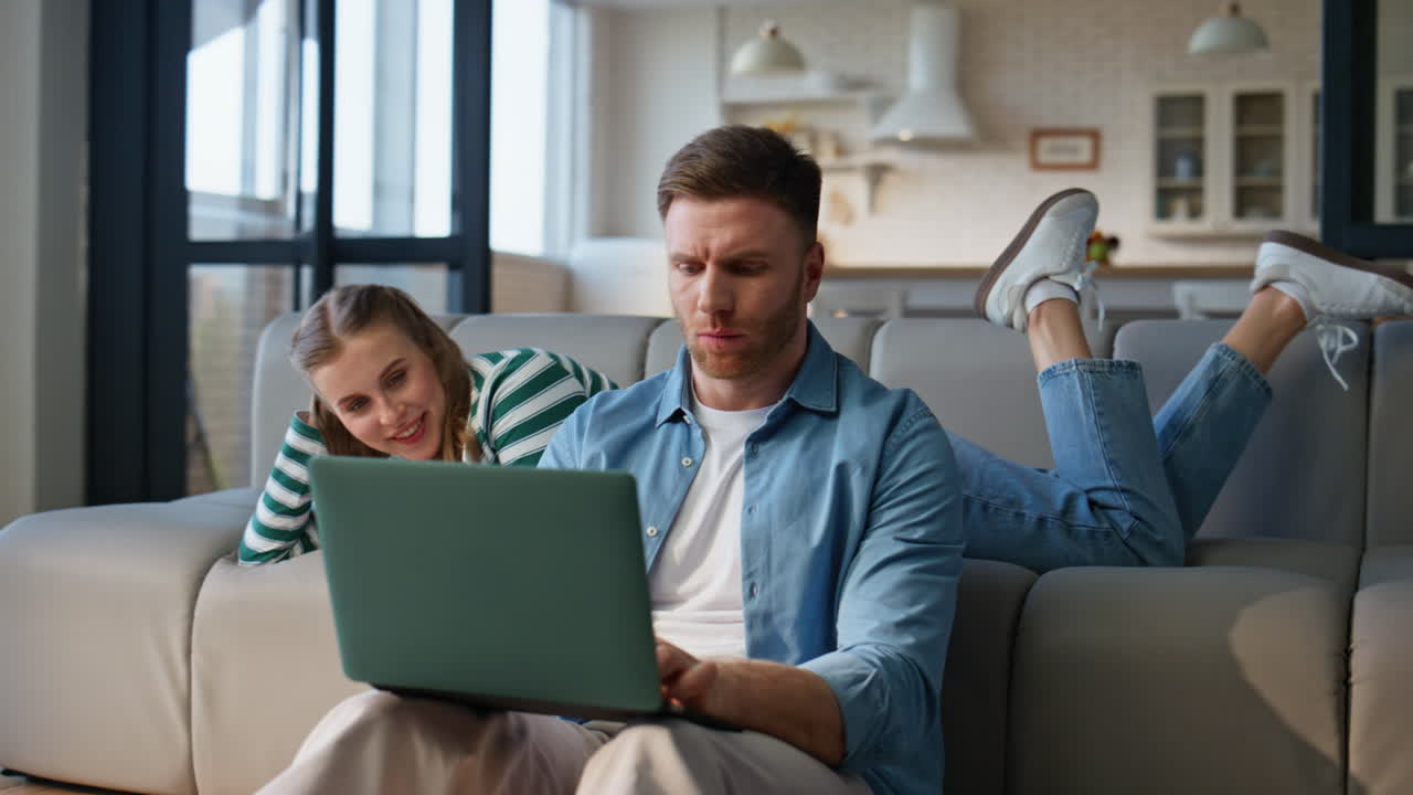 Focused boyfriend working laptop girlfriend leaning at sofa. Man solving tasks