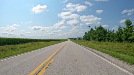 pov - driving on a country road past rural subdivision and crops in fields in late summer in central iowa