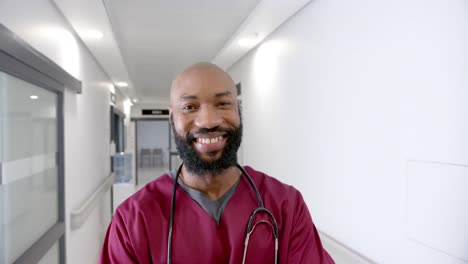 Porträt-Eines-Glücklichen-Afroamerikanischen-Männlichen-Arztes-Im-Krankenhausflur,-Zeitlupe